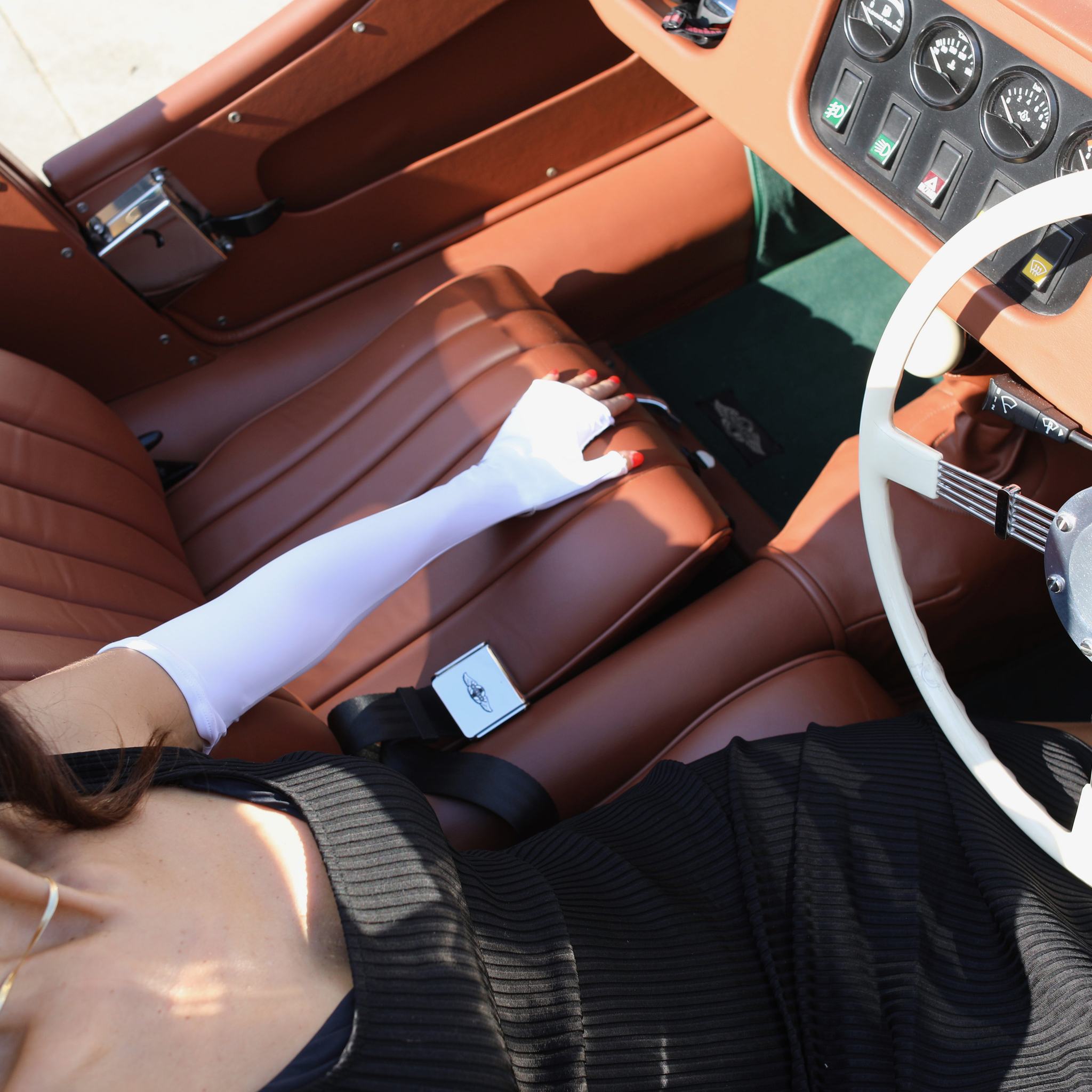 Woman sitting in a vintage car wearing long white UPF 50+ (sun protective) gloves.