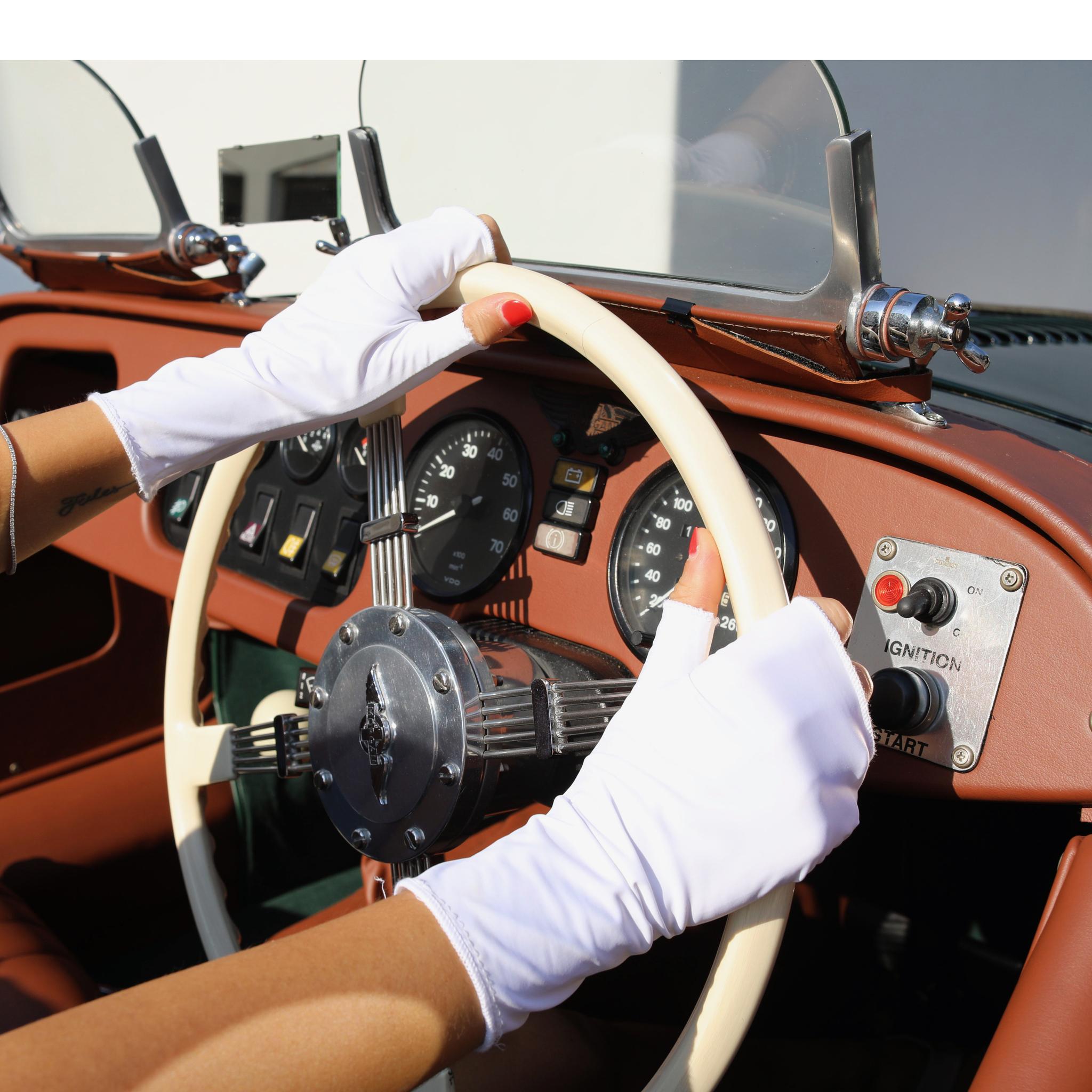Woman holding a car steering wheel wearing short white UPF 50+ (sun protective) gloves for hand protection.