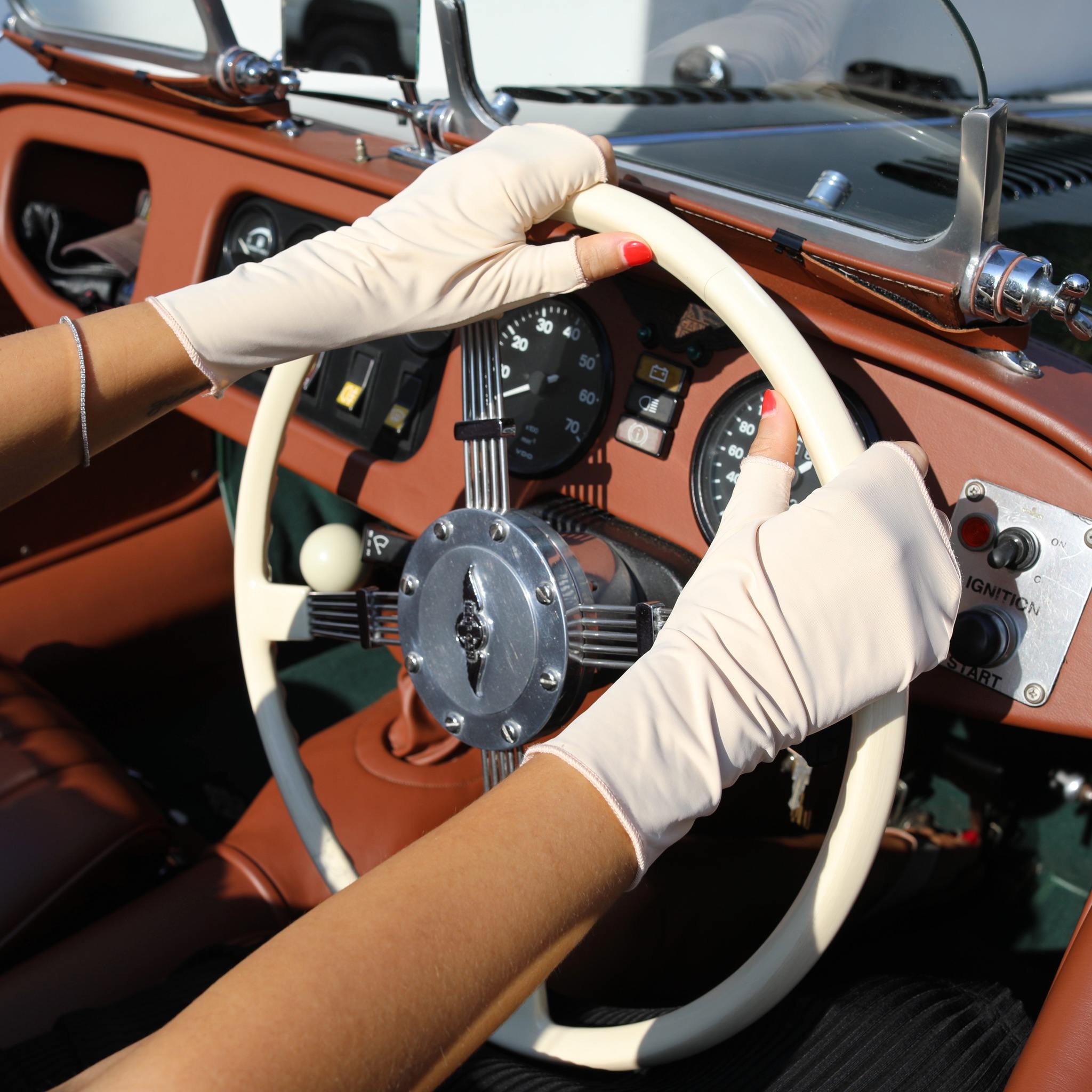 Woman holding a car steering wheel wearing short nude UPF 50+ (sun protective) gloves.