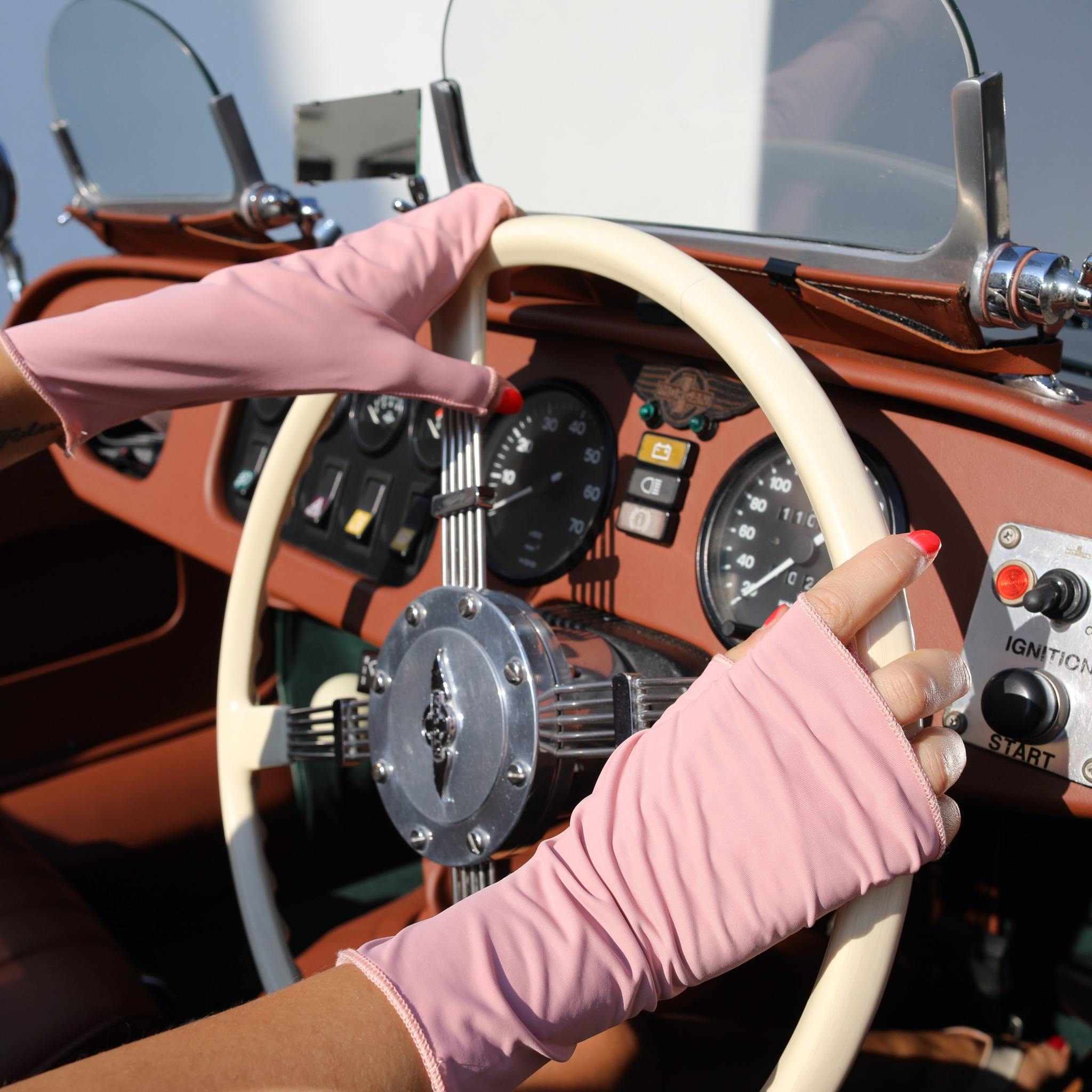 Woman holding a car steering wheel wearing pink UPF 50+ (sun protective) gloves.