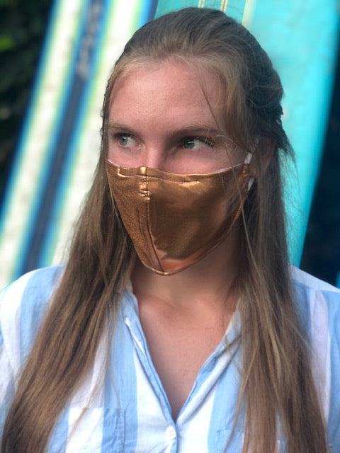 Woman in front of surfboards wearing a gold face mask.