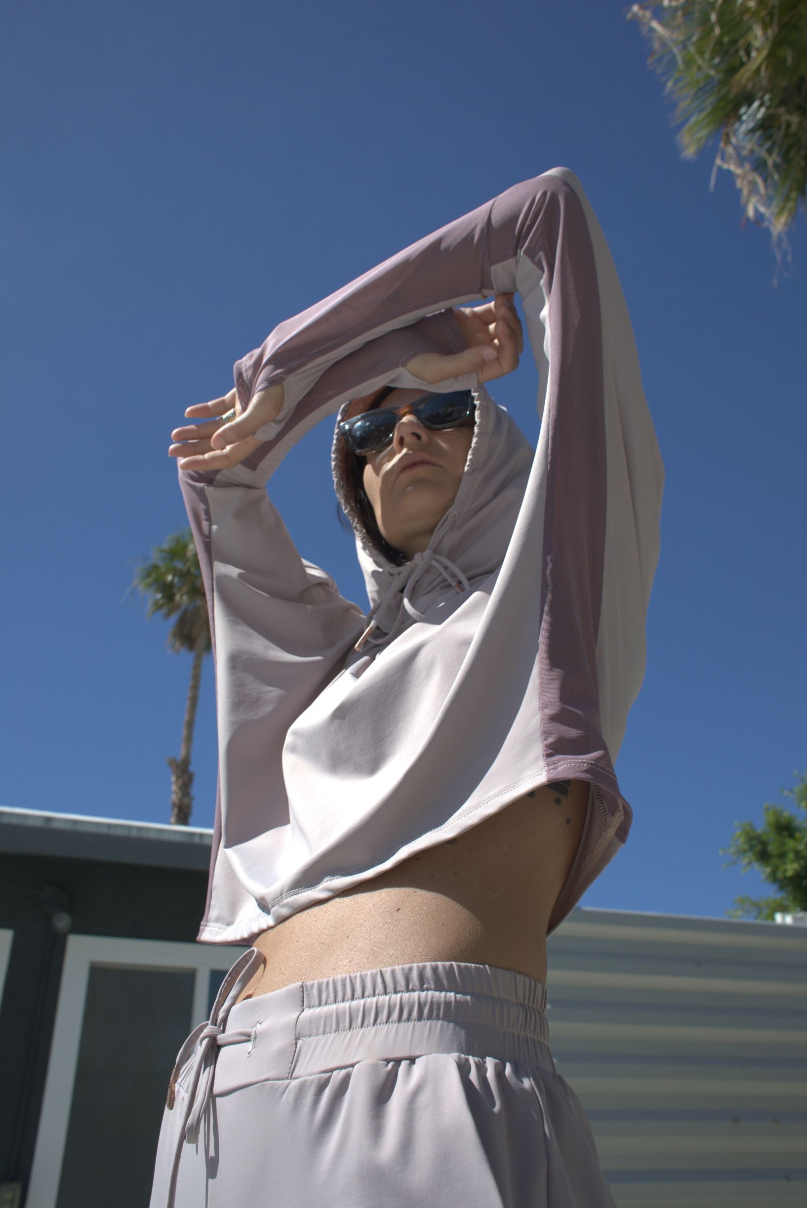 Woman wearing a lightweight, long sleeved sun protective hoodie with hand coverings and matching UPF 50+ drawstring pants in iris.