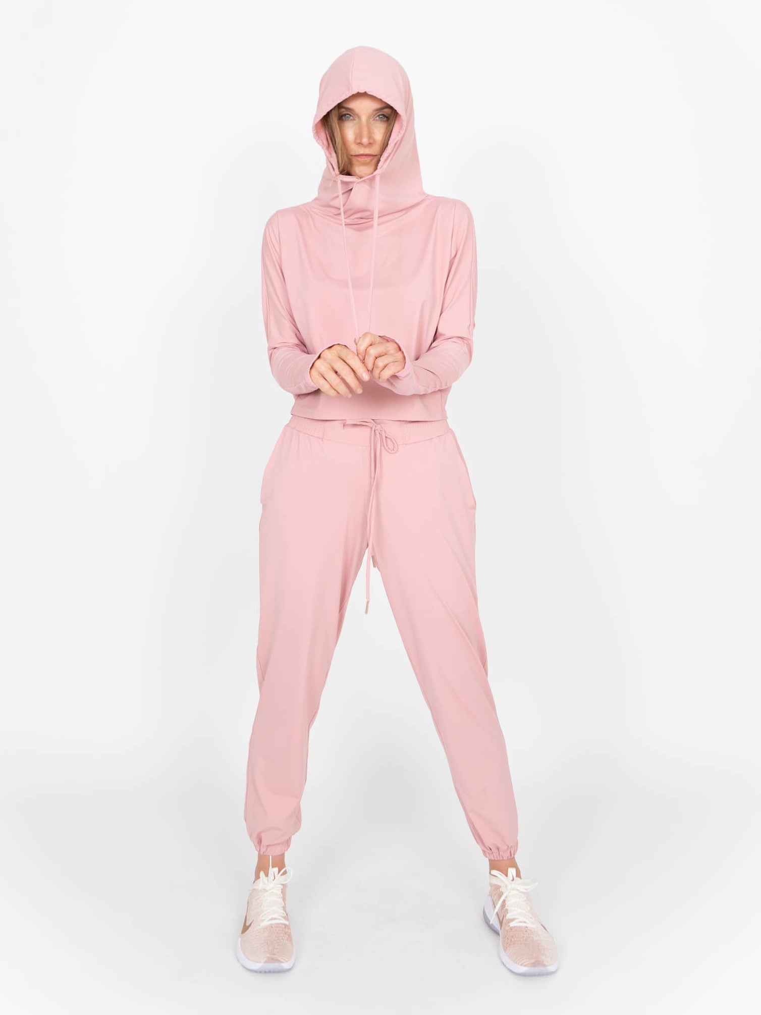Woman wearing a lightweight long sleeved sun protective hoodie with hand coverings in blush pink and matching drawstring pants.