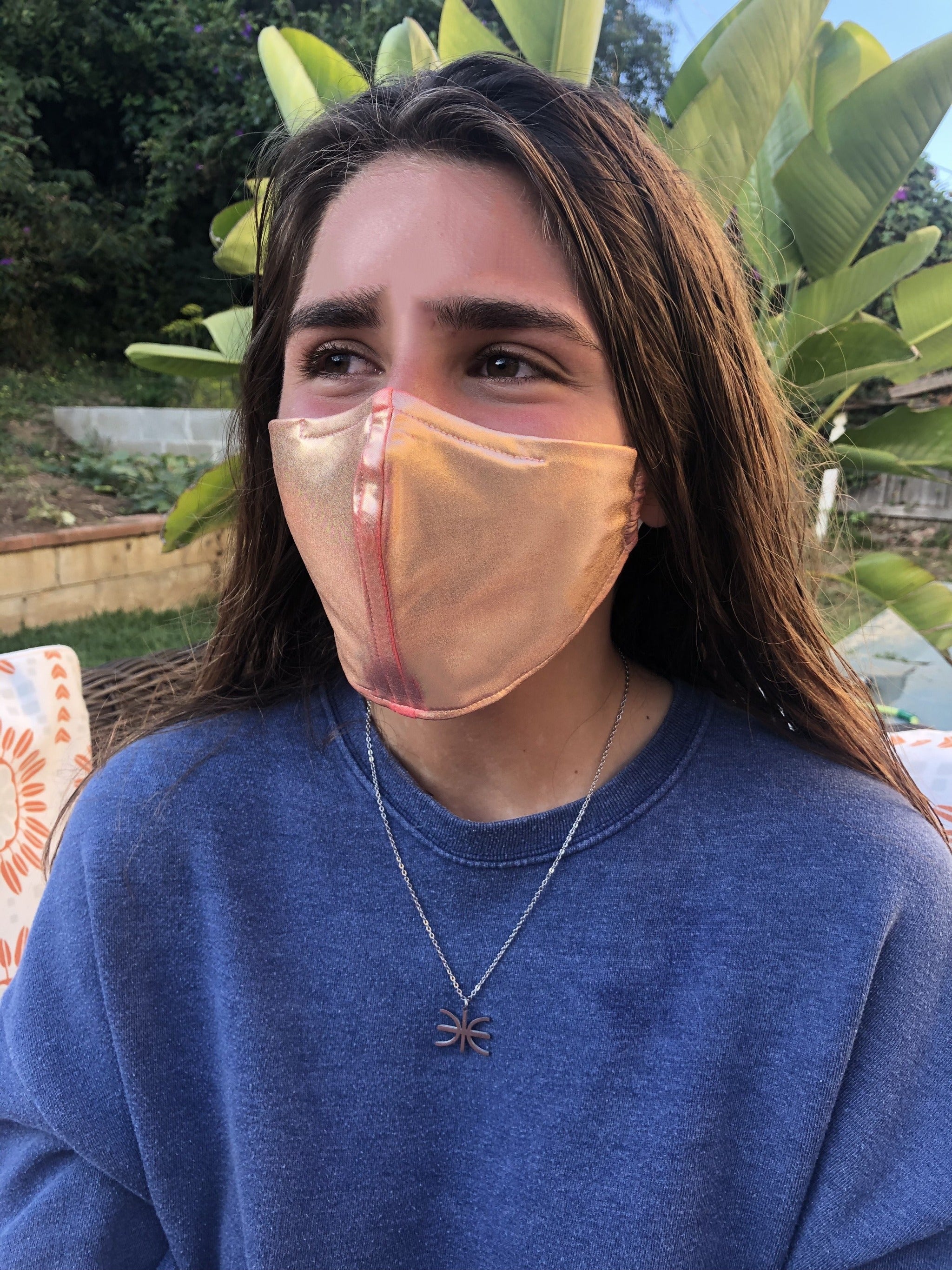 Girl in front of a palm tree wearing a rose gold face mask.
