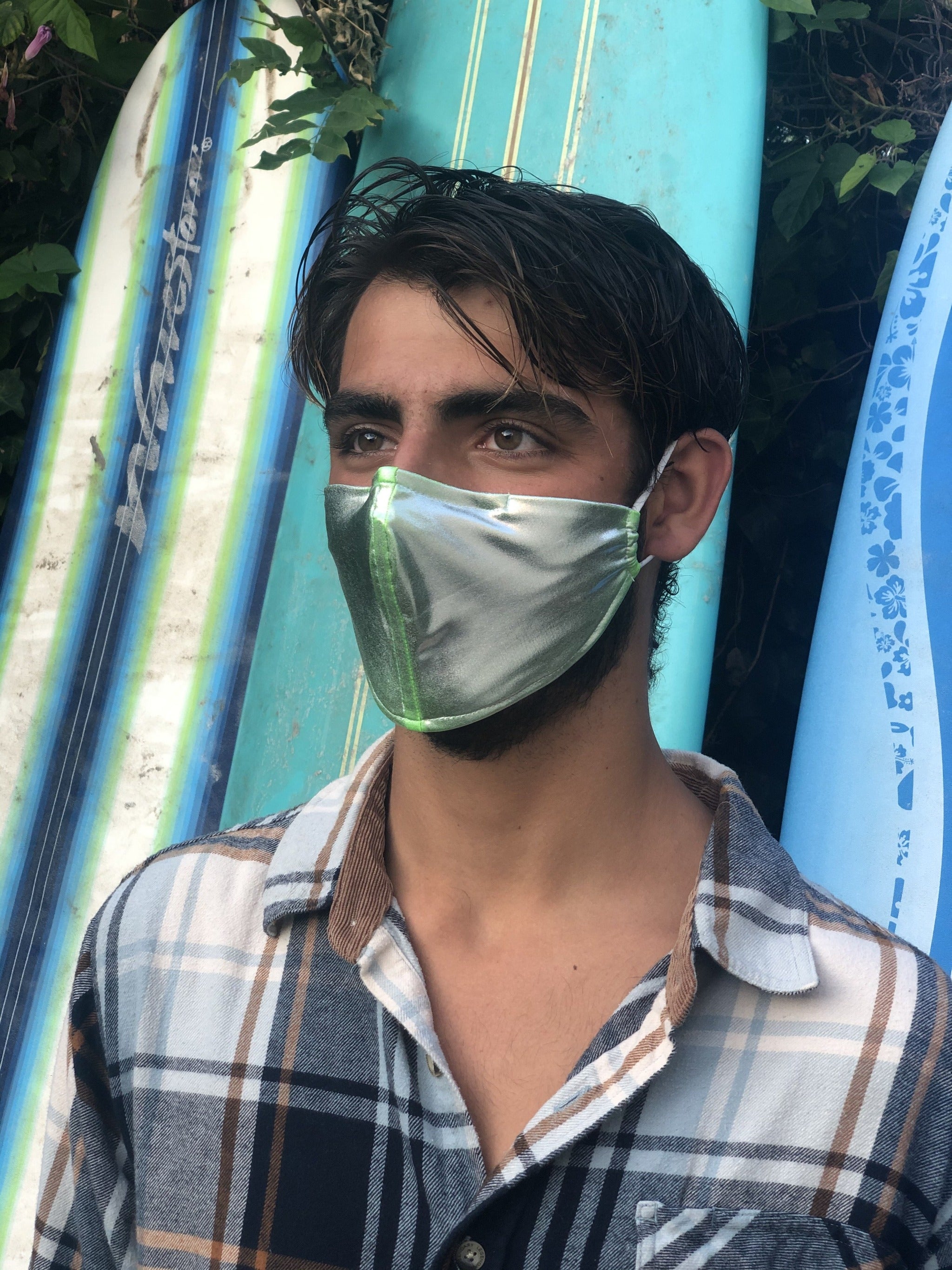 Man in front of surfboards wearing a silver face mask.