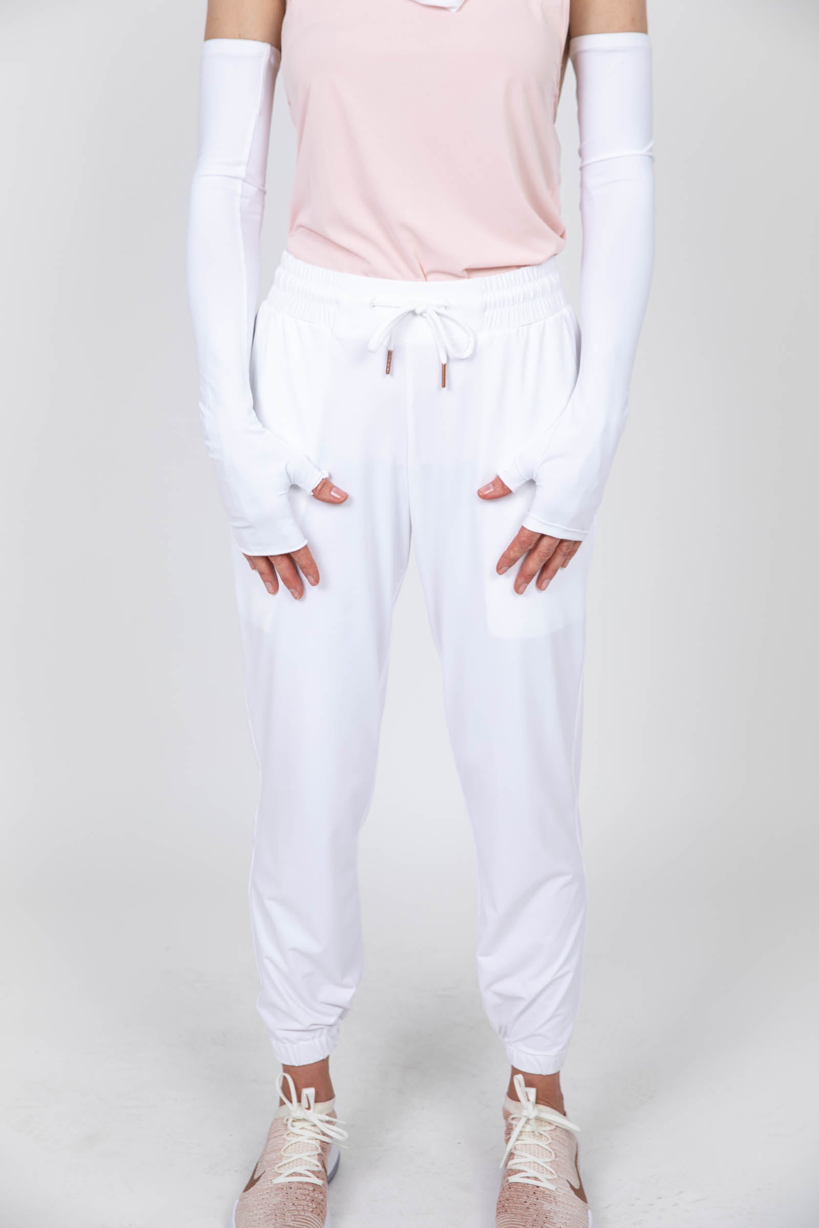 Woman wearing long sun protective gloves and drawstring pants in white.