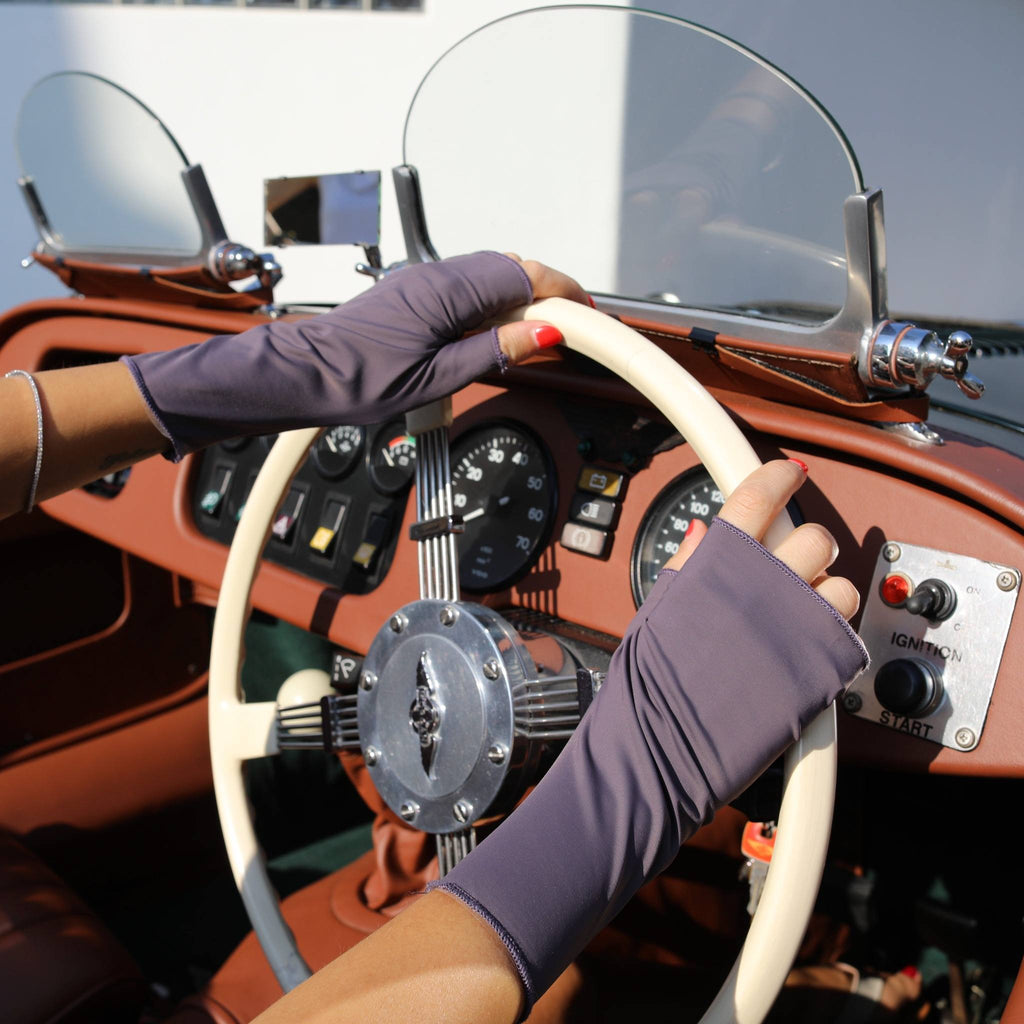Woman holding a car steering wheel wearing short UPF 50+ (sun protective) gloves in plum. 