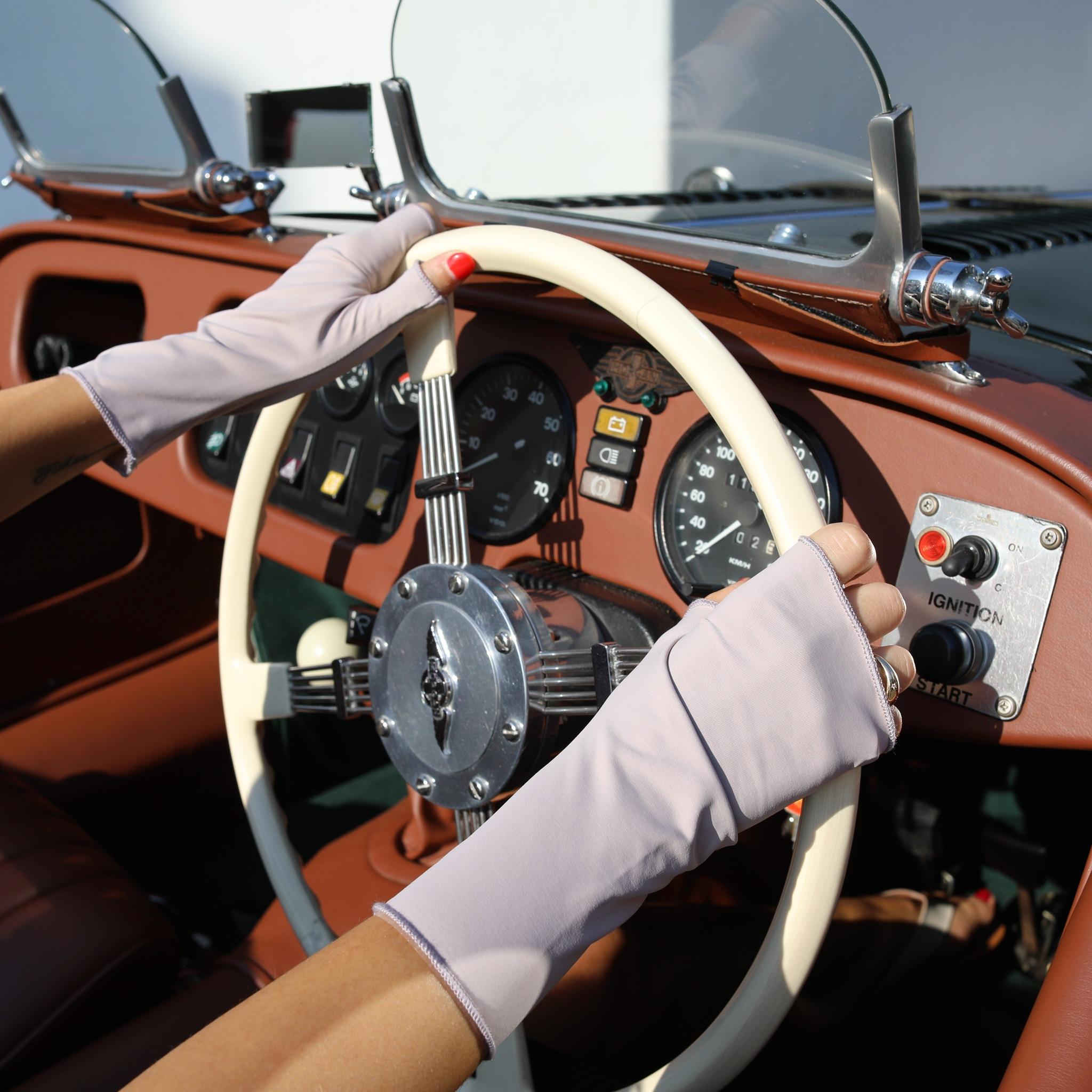 Woman holding a car steering wheel wearing UPF 50+ (sun protective) gloves for hand protection in iris.