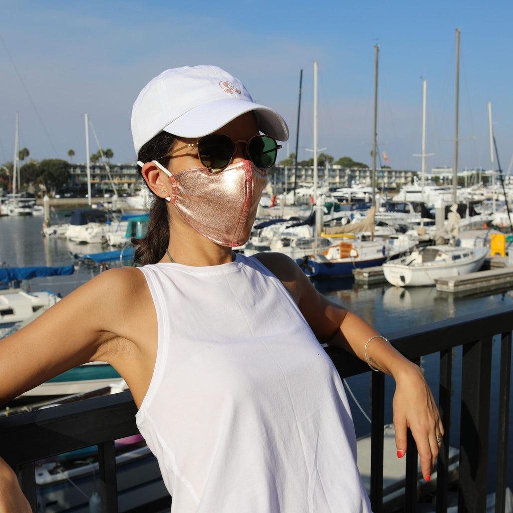 Woman in a sunny boat-filled marina wearing a rose gold face mask.