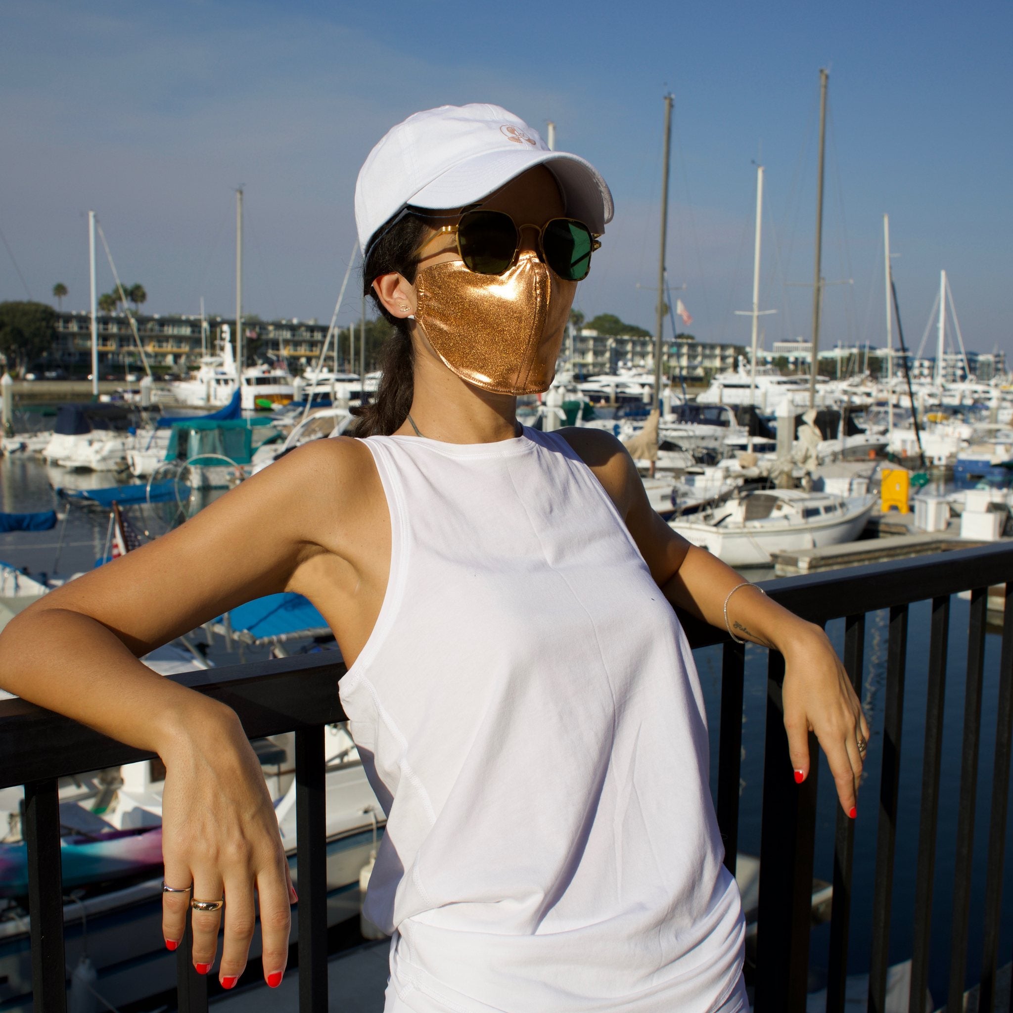 Woman in a sunny boat-filled marina wearing a gold face mask.