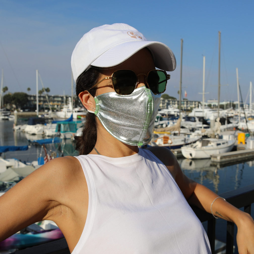 Woman in a sunny boat-filled marina wearing a silver face mask.