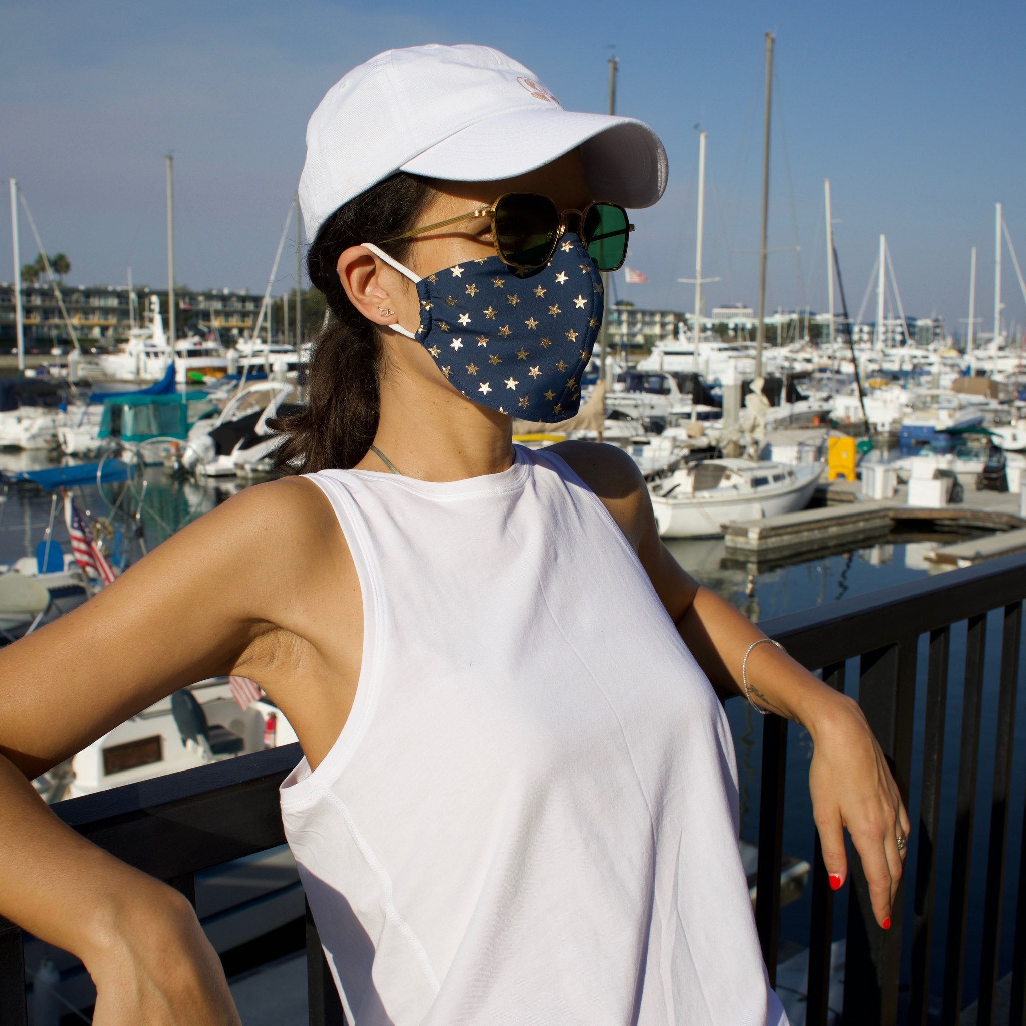 Woman in a sunny boat-filled marina wearing a blue face mask with gold stars.