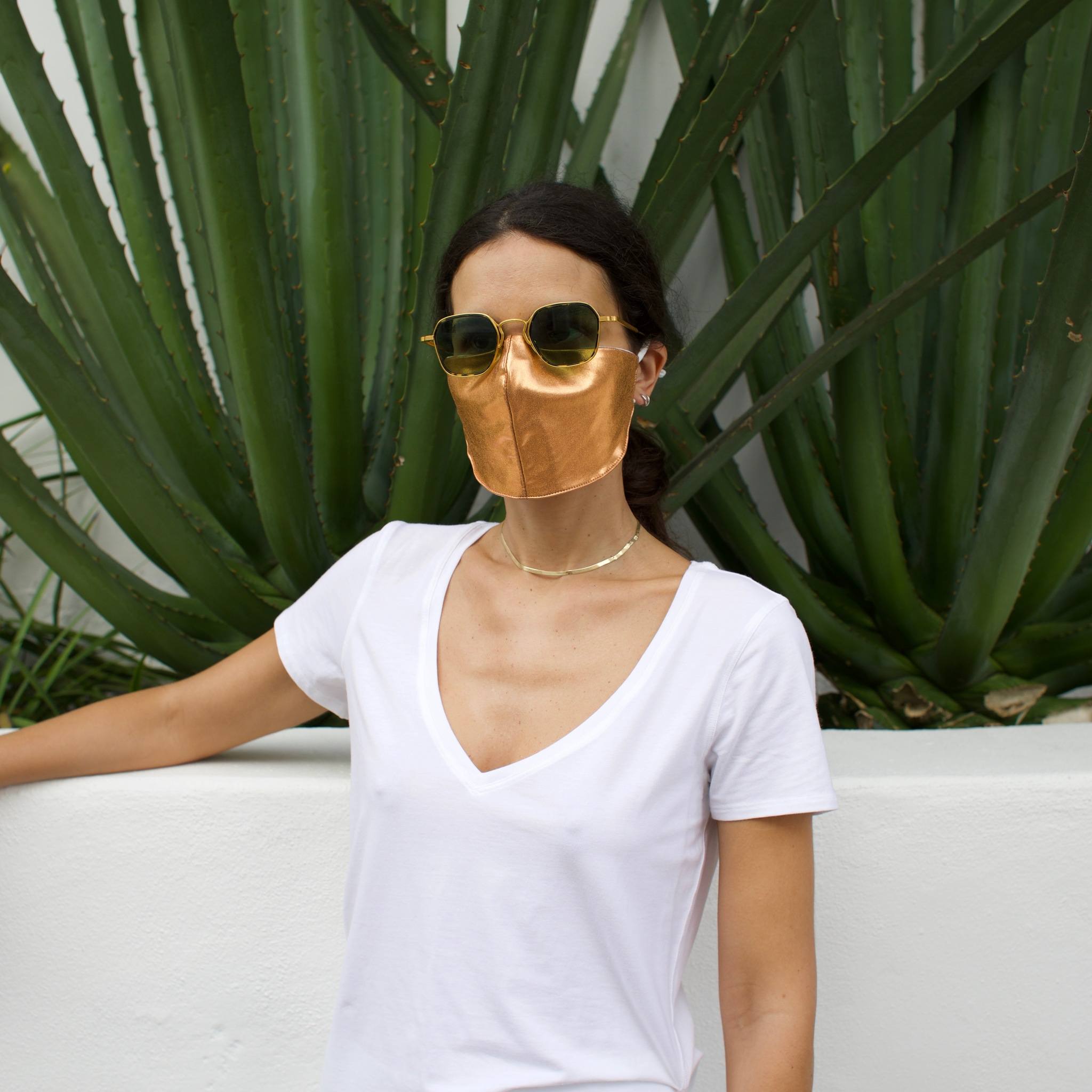 Woman in front of a cactus wearing a gold face mask.