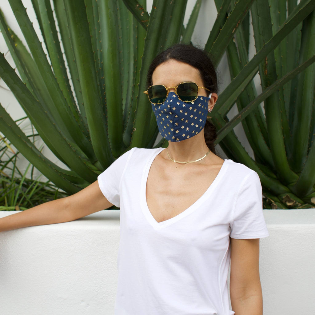 Woman in front of a cactus wearing a blue face mask with gold stars.