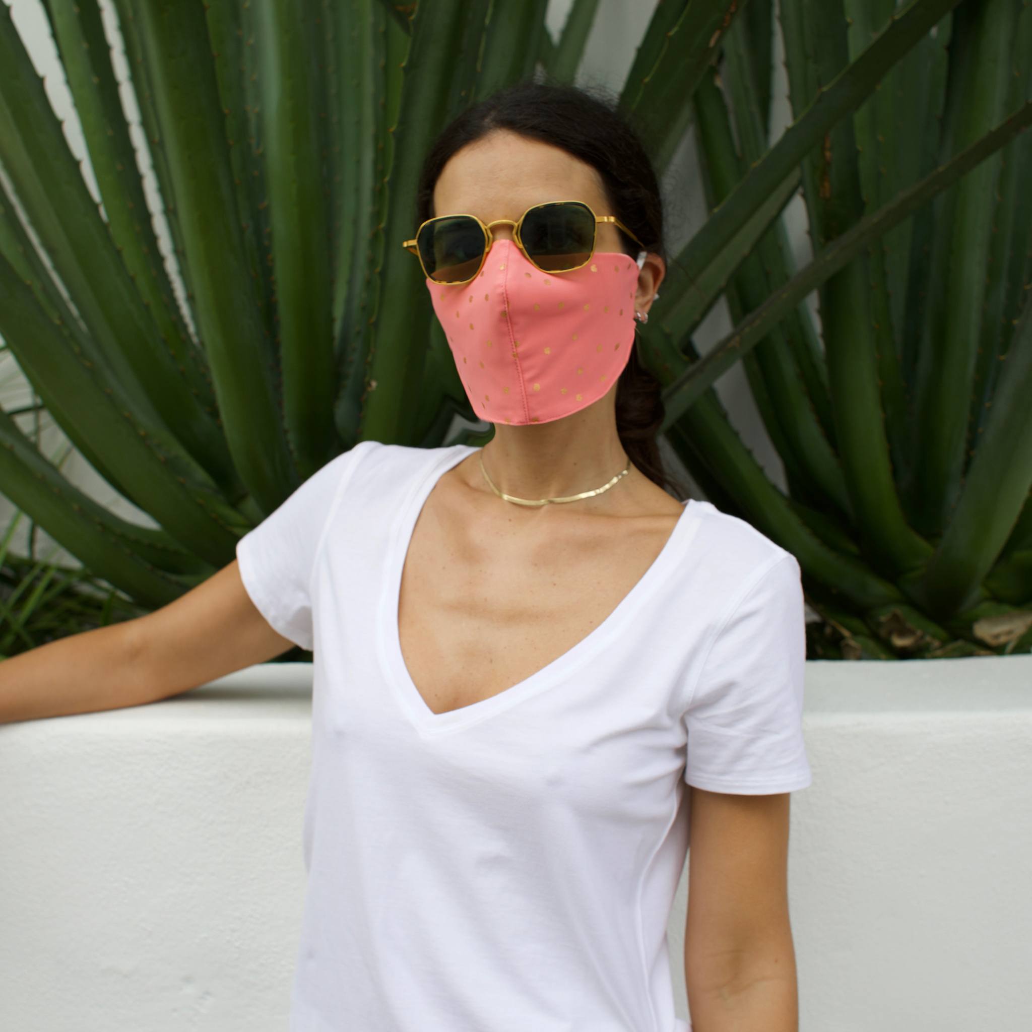 Woman in front of a cactus wearing a pink face mask with gold polka dots.