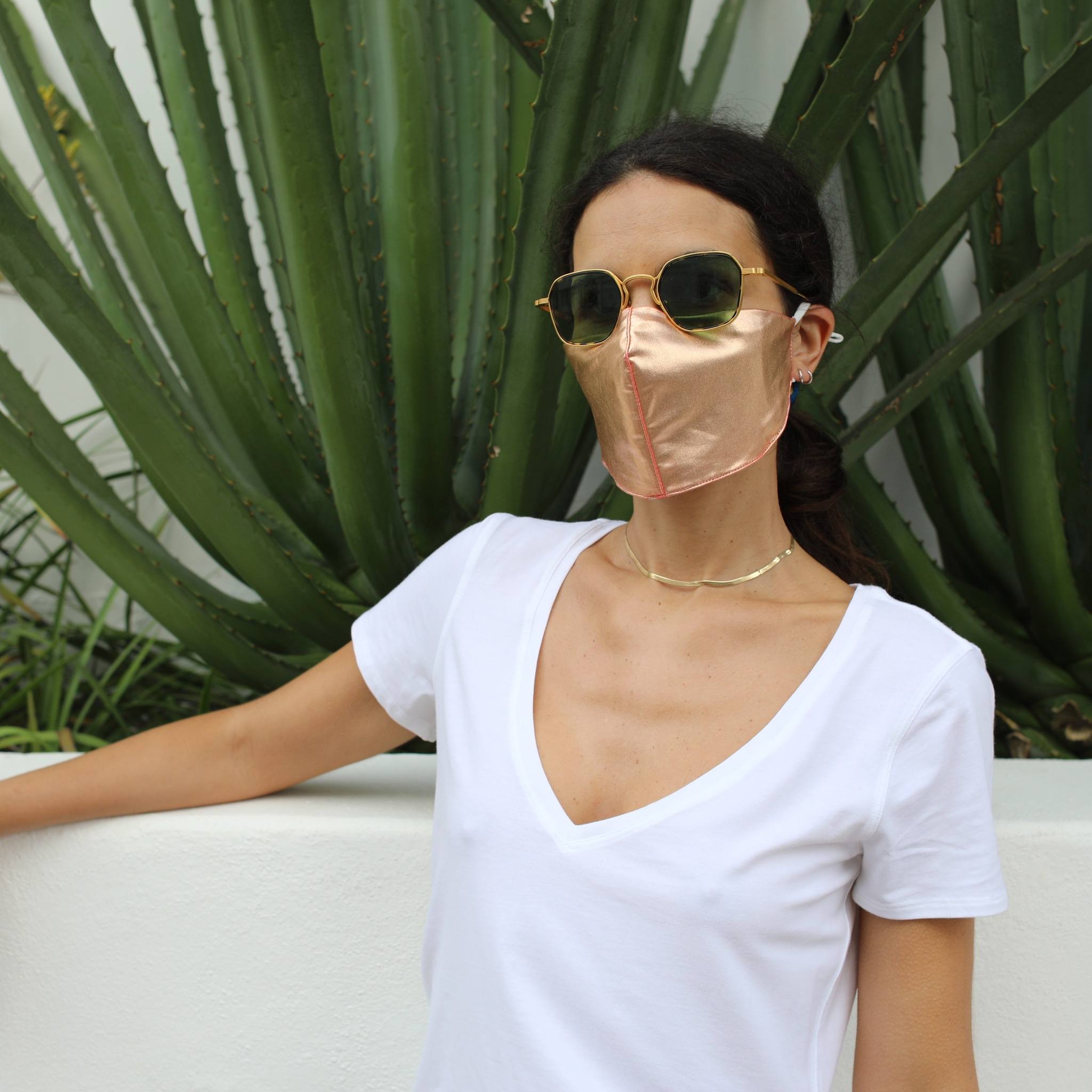 Woman in front of a cactus wearing a rose gold face mask.