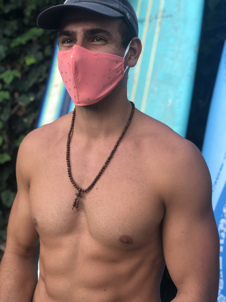 Shirtless man with surfboards wearing a pink face mask with gold polka dots.