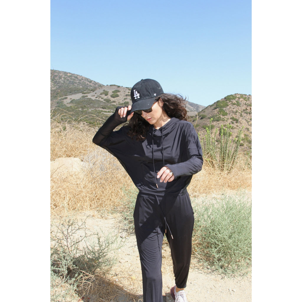 Woman outdoors wearing a lightweight, long sleeved sun protective black hoodie with hand coverings and matching UPF 50+ drawstring pants.