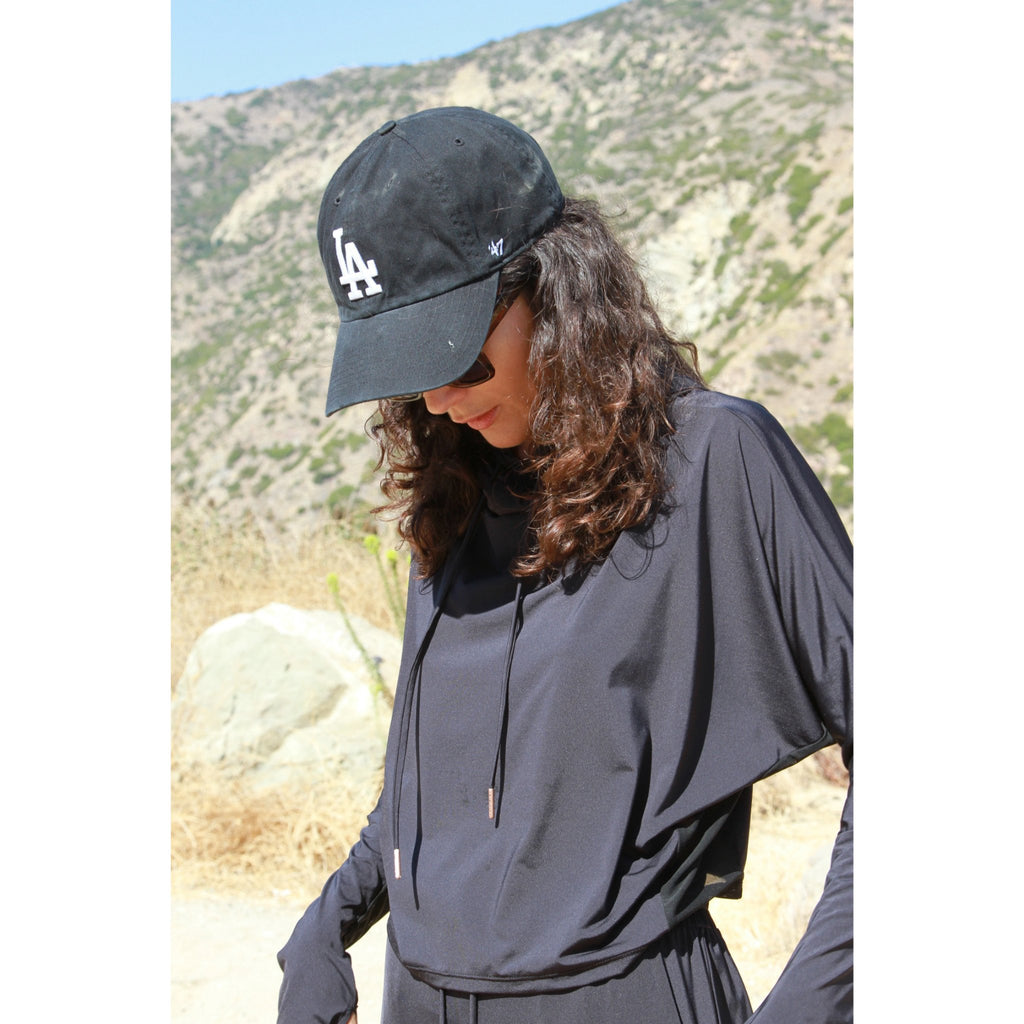 Woman outdoors wearing sunglasses and a soft, long sleeved sun protective black hoodie with hand coverings and matching UPF 50+ drawstring pants.