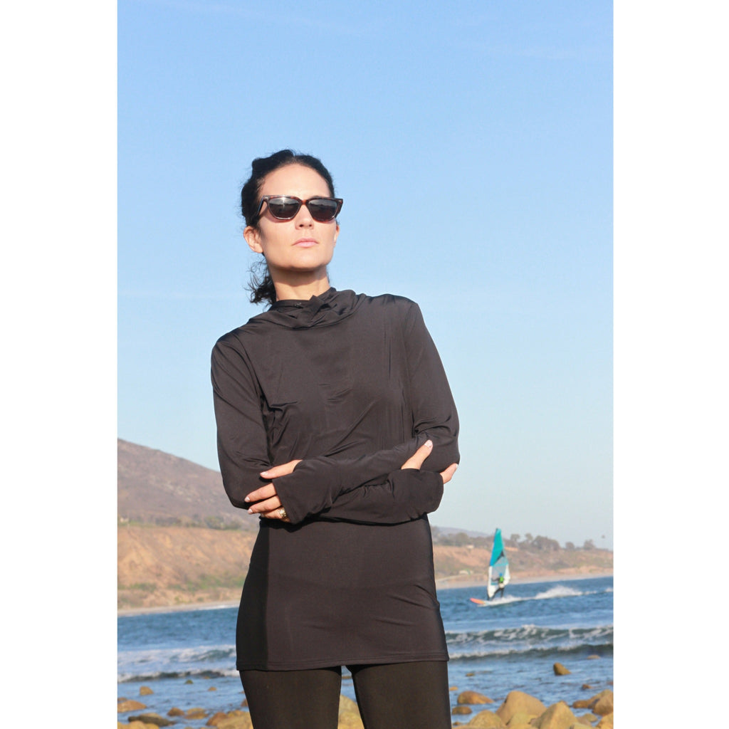 Woman on a beach wearing a long-sleeved UPF 50+ (sun protective) shirt with full hood and hand protection in black.