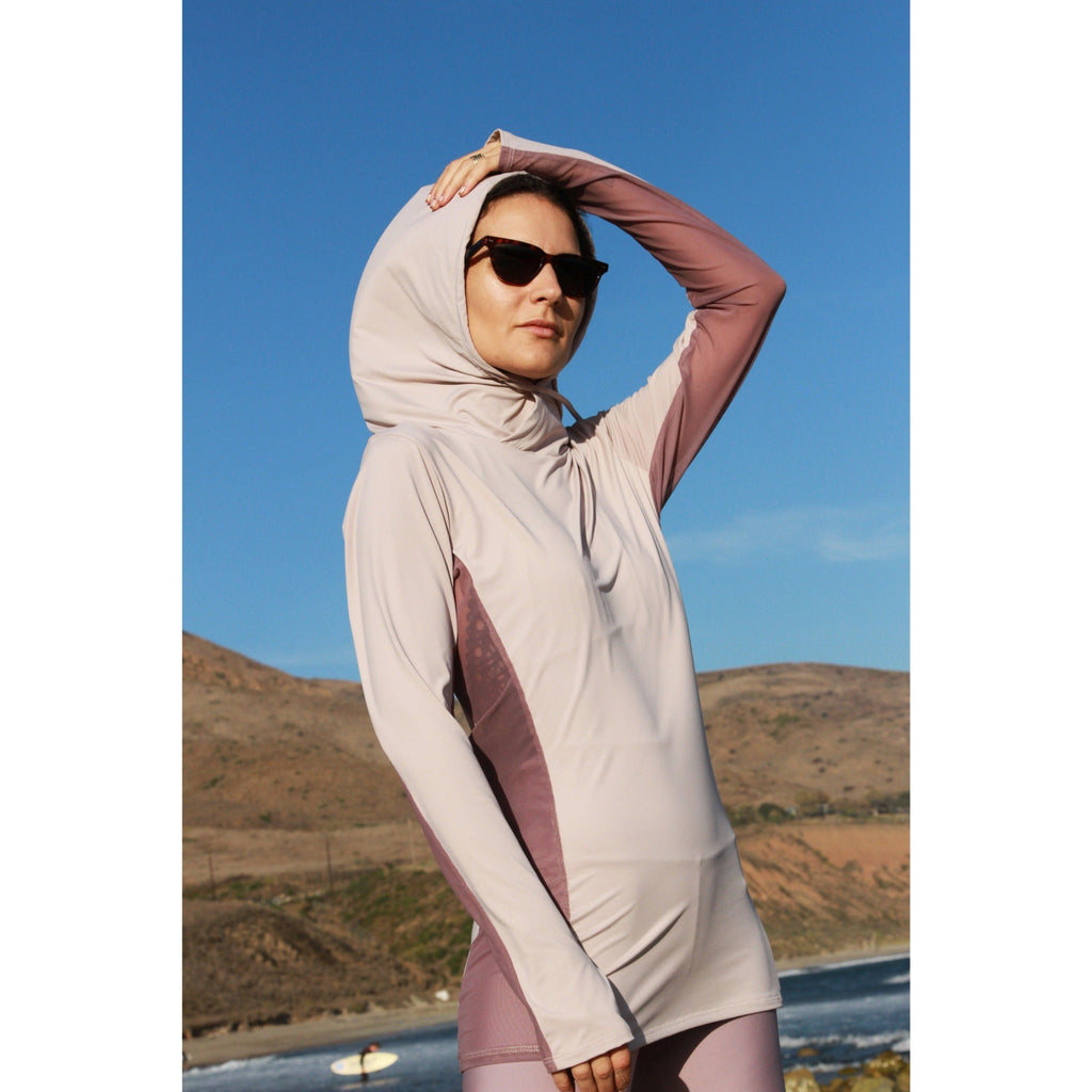 Woman on a beach wearing a long-sleeved sun protective shirt with full hood and hand protection in iris.