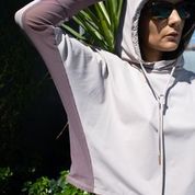 Woman wearing a lightweight, long sleeved sun protective hoodie with hand coverings in iris. 