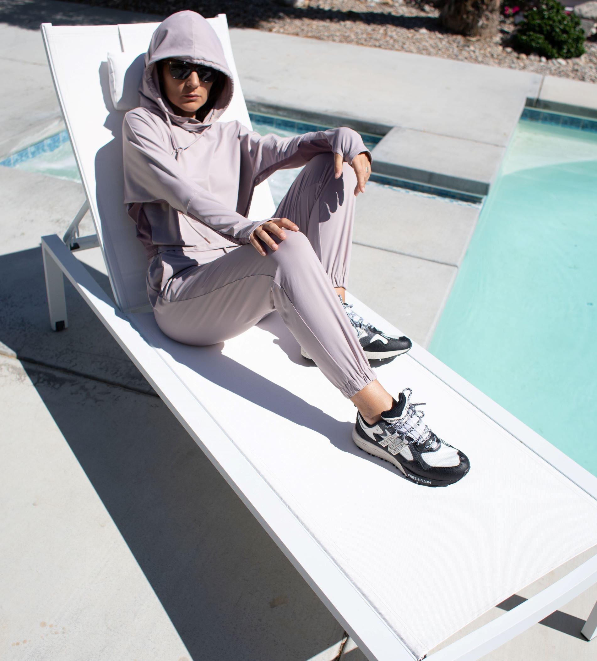 Woman poolside wearing a light weight long sleeved sun protective hoodie with hand coverings in and matching drawstring pants in iris.