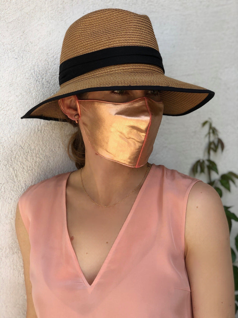 Woman in front of a white wall wearing a rose gold face mask.