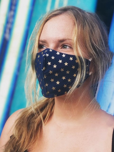 Woman in front of surfboards wearing a blue face mask with gold stars.