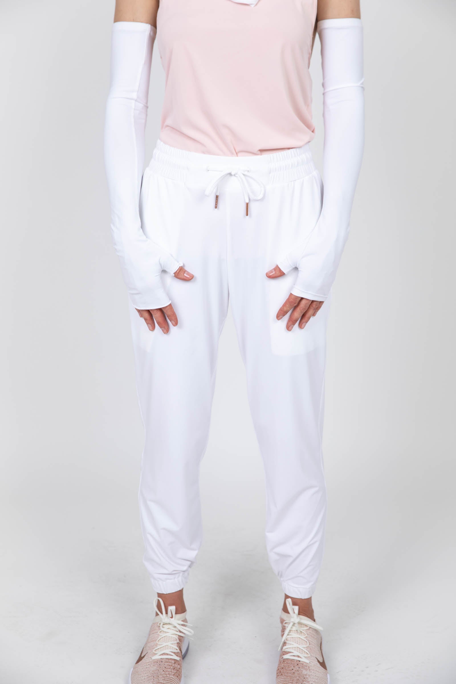 Woman wearing long sun protective gloves and drawstring pants in white. 